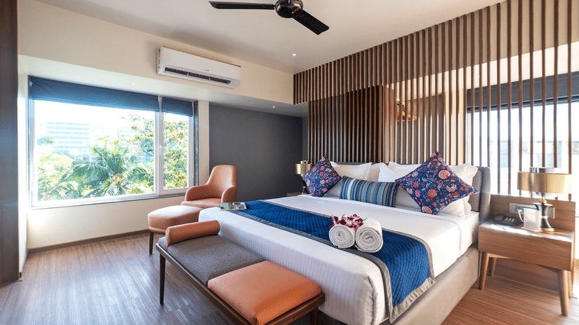 Studio Suite at Hotel Le Grande with a large bed, stylish décor, lounge chair by a sunny window, and contemporary wooden accents throughout.