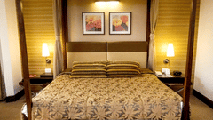 A bedroom with a four-poster bed, two side tables with lamps, framed wall art, and warm lighting.