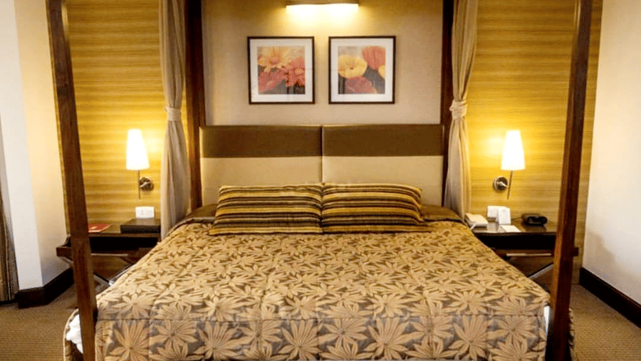 A bedroom with a four-poster bed, two side tables with lamps, framed wall art, and warm lighting.