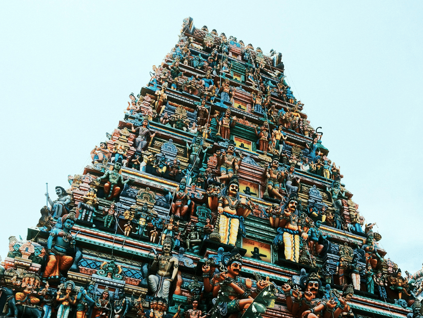 A view from below of a temple with layered architecture featuring numerous deities on each layer and the entrance at the bottom..