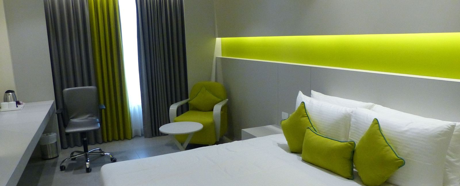  Spacious twin beds with headboards line the wall, large windows with curtains cover them, and a sofa is placed near the window
