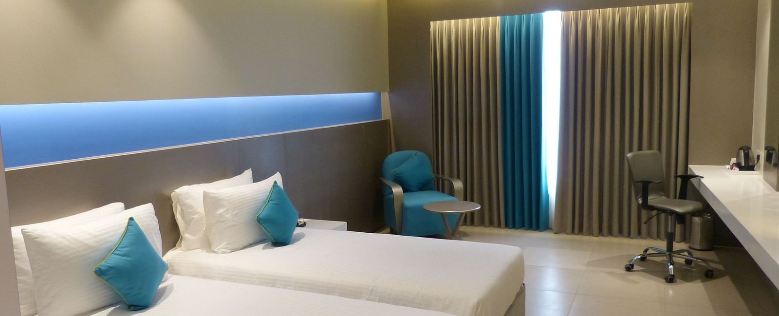  Spacious twin beds with headboards stretch across the wall, and large windows with curtains cover them