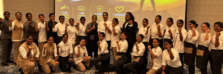 Female staff members of The Residency Hotels posing together with raised fists in front of a projection screen reading 'I AM STRONG'.