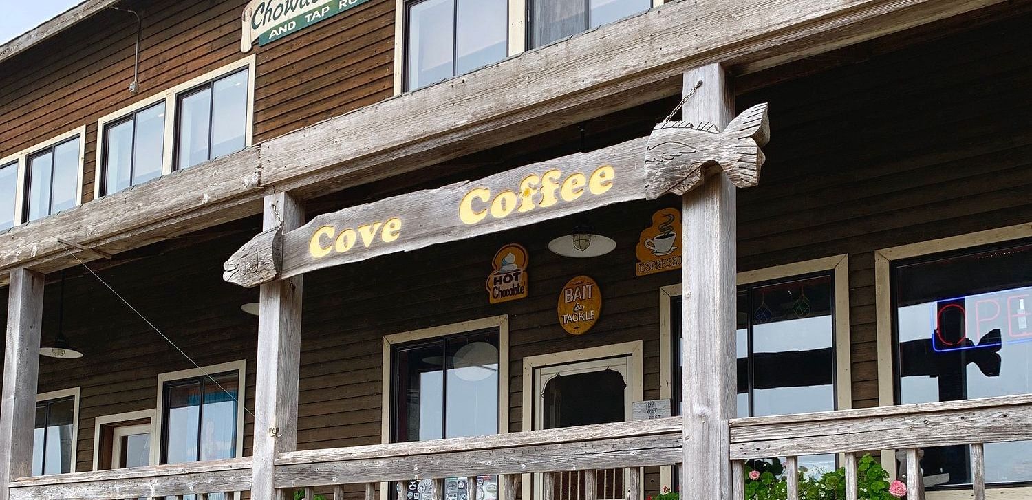 A building with a covered porch featuring a Cave Coffee sign, a railing, and multiple windows.