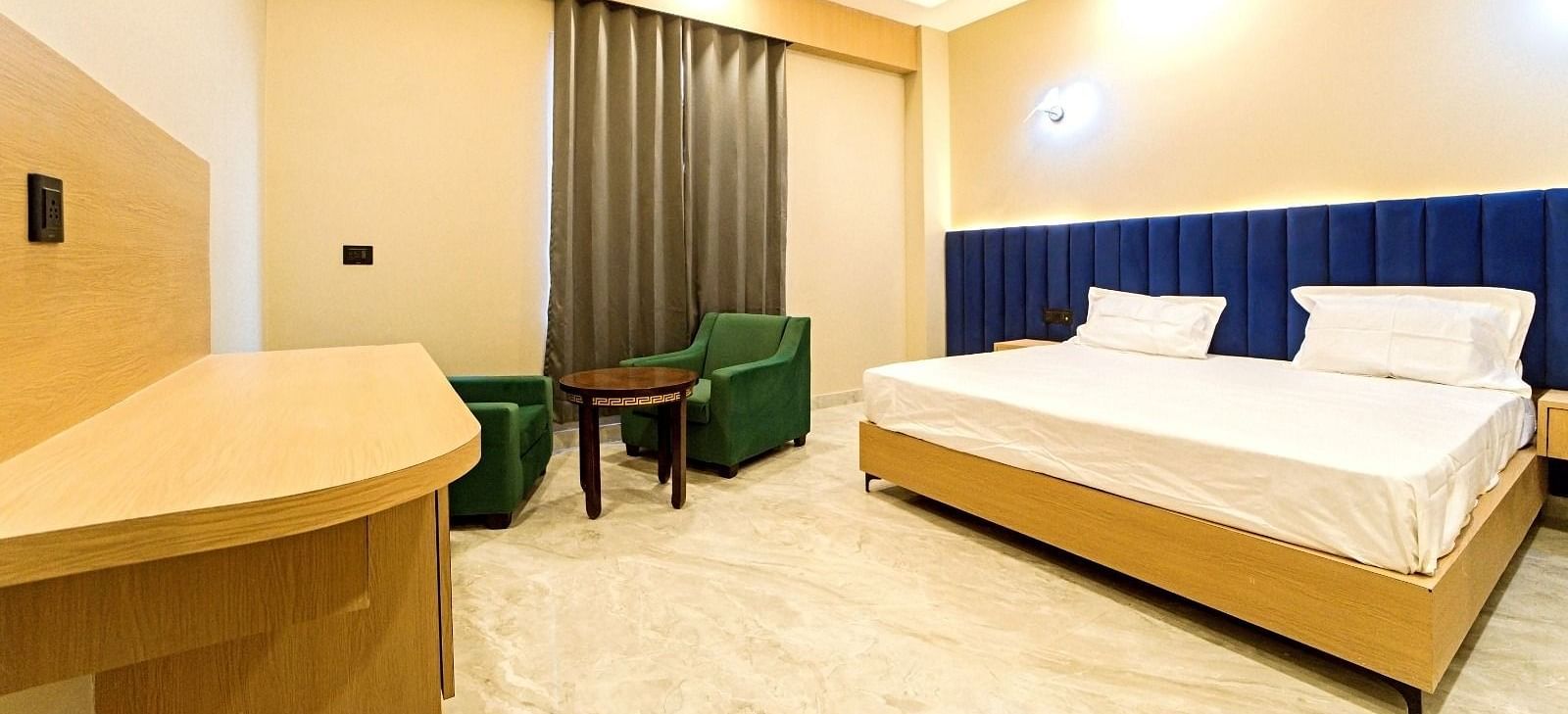 Modern guest room at Grassfield Riveria Resort, Jaipur, featuring a large bed, seating area, ceiling fan, and warm lighting.