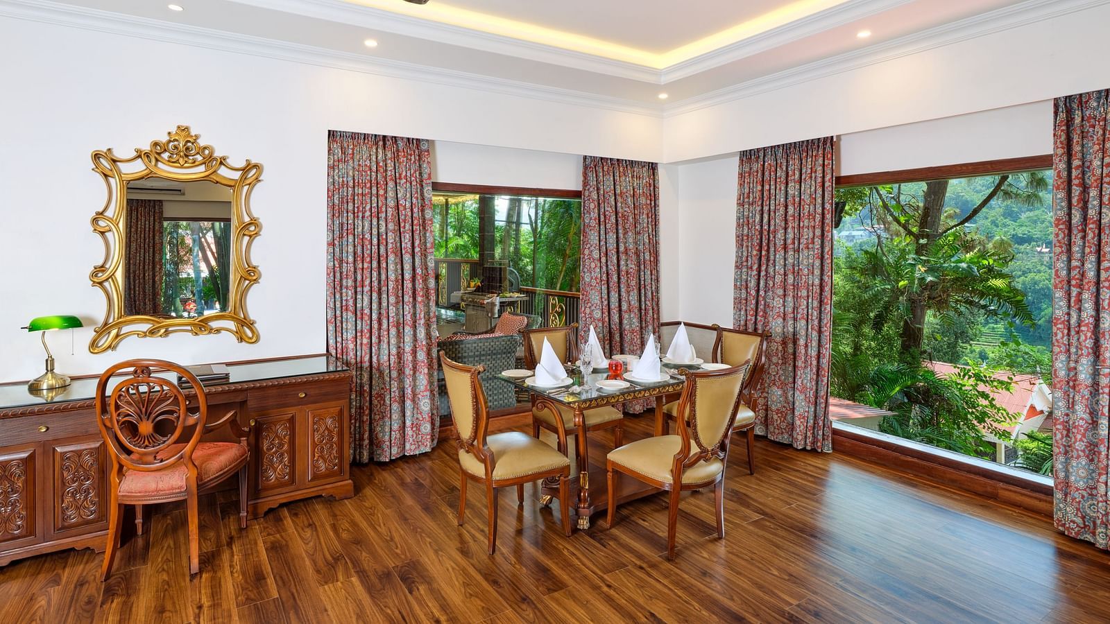 A room with a dining table and four chairs surrounding it with a cupboard, ceiling fan. mirror, and curtained windows  at Mayfair Spa Resort and Casino.