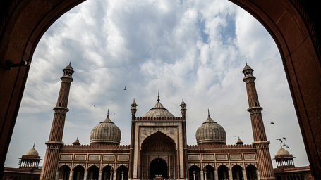 Grand view of Jama Masjid, one of the well-known Weekend Places in Delhi to visit, framed through a stone archway, highlighting its domes, minarets, and striking Mughal architecture beneath cloudy skies