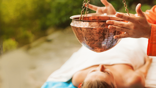 A person lying on their back while a couple of hands holding a hanging pot