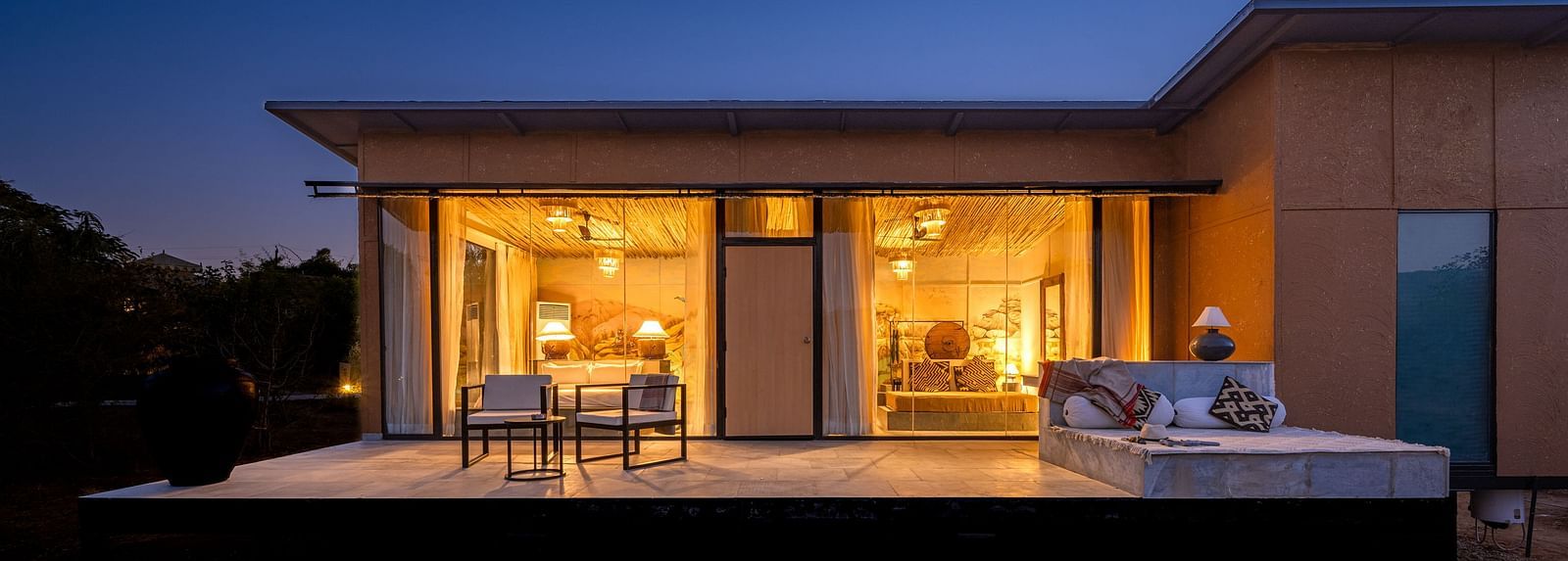 A facade view of a room with bright lighting and greenery around - Utsav Camp Sariska.