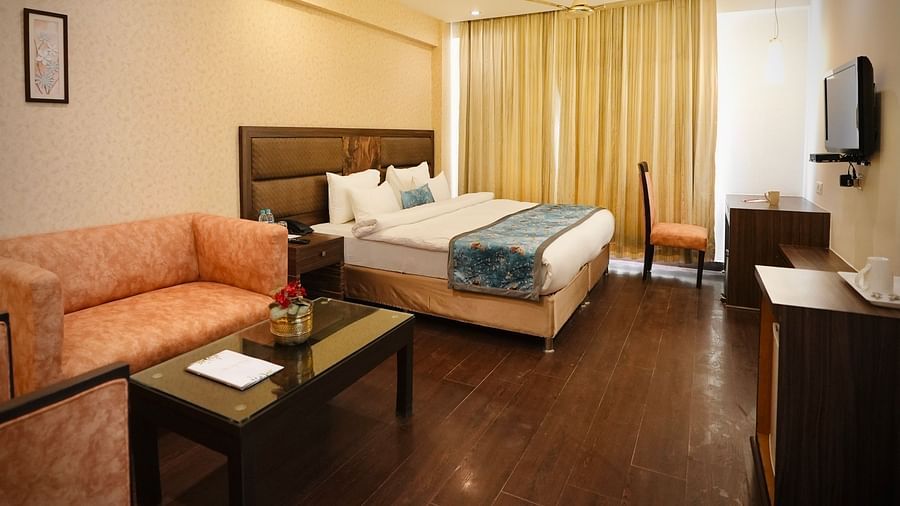 A bedroom with a neatly made bed, a peach-coloured sofa, and a small table, creating a comfortable space - VITS Gurugram