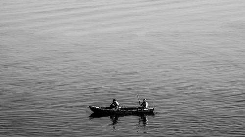 A small boat with two people rowing on calm water in a wide view.