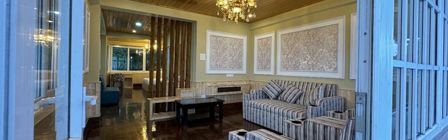 An image of a seating room which has a seating area like sofa, centre table. Chandelier hung from a wooden ceiling - Avianna Group of Hotels & Resorts