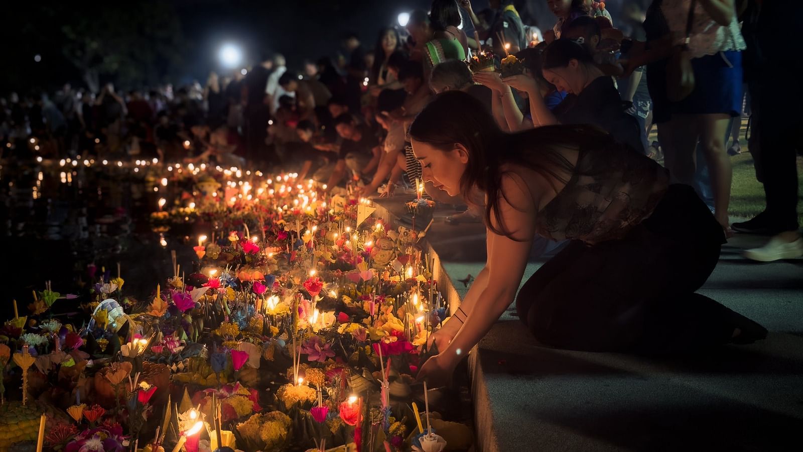 a woman participating in Loy Krathong Celebrations by placing a floating lantern on the waterbody