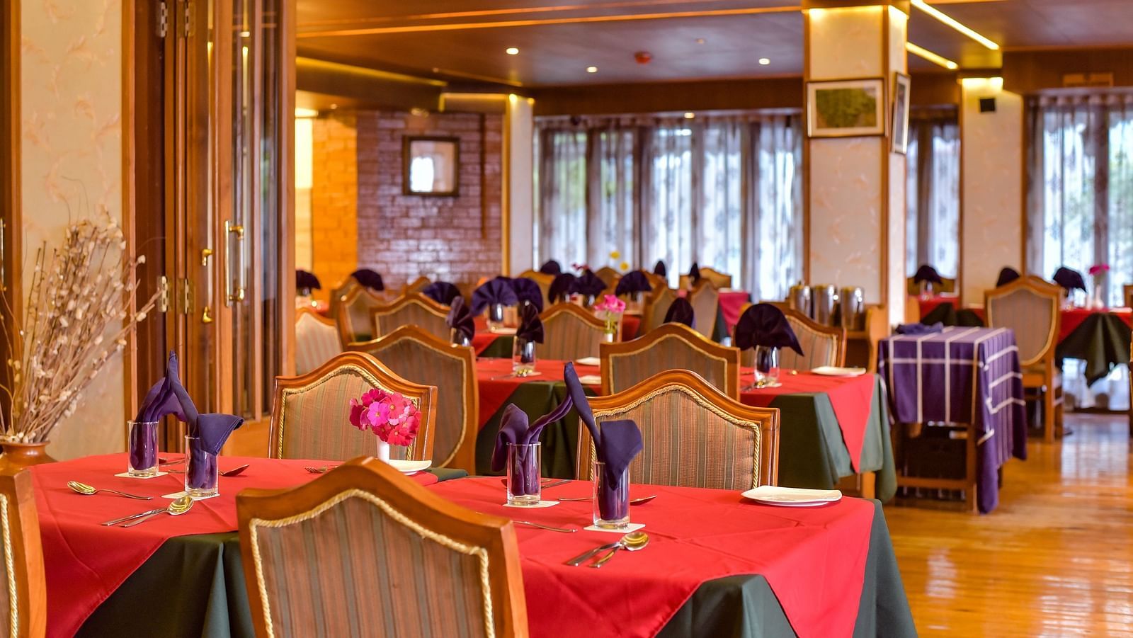 Dining area at Cedar Inn, Darjeeling, featuring elegant wooden interiors, red and green tablecloths, and neatly folded napkins on each table.