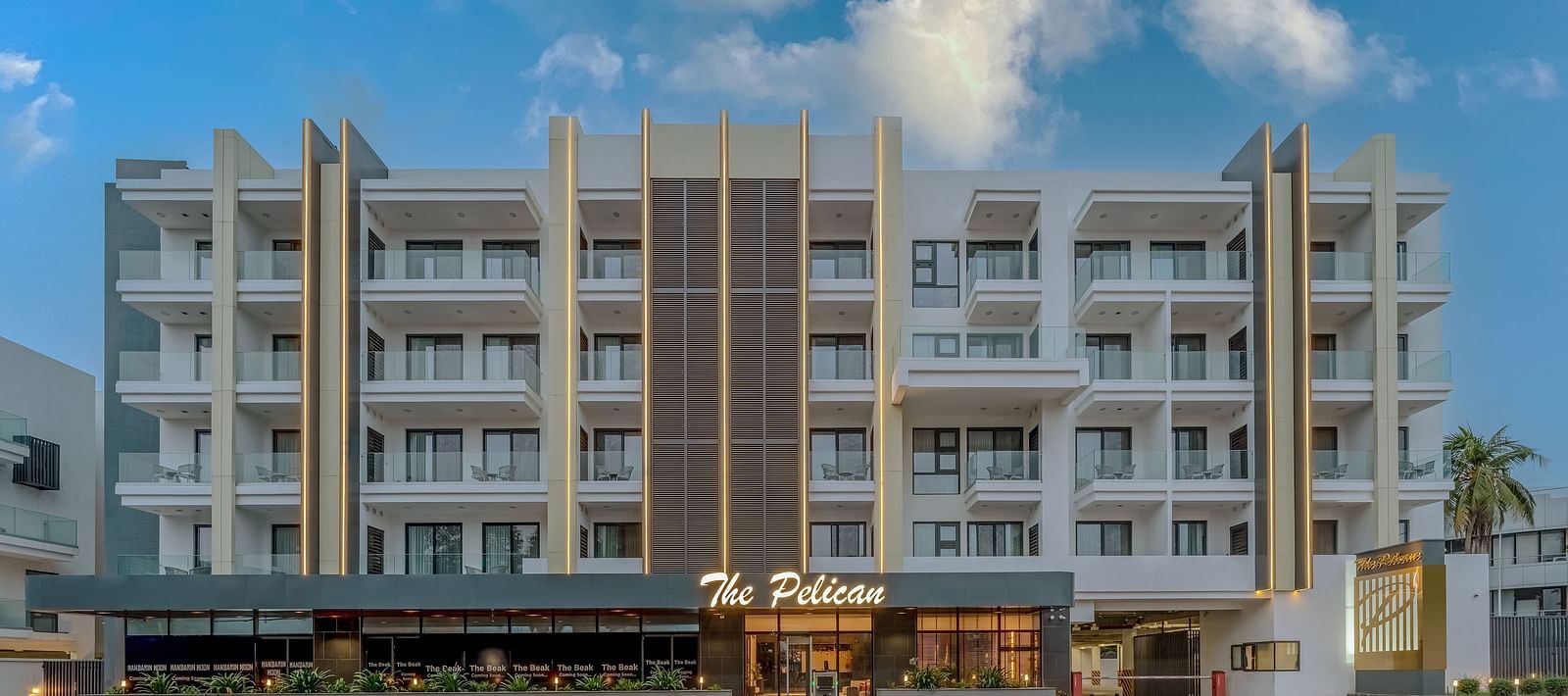A tall white hotel building with palm trees in front and a clear blue sky in the background - The Pelican Hotel, Accra - Accra Hotel Images.
