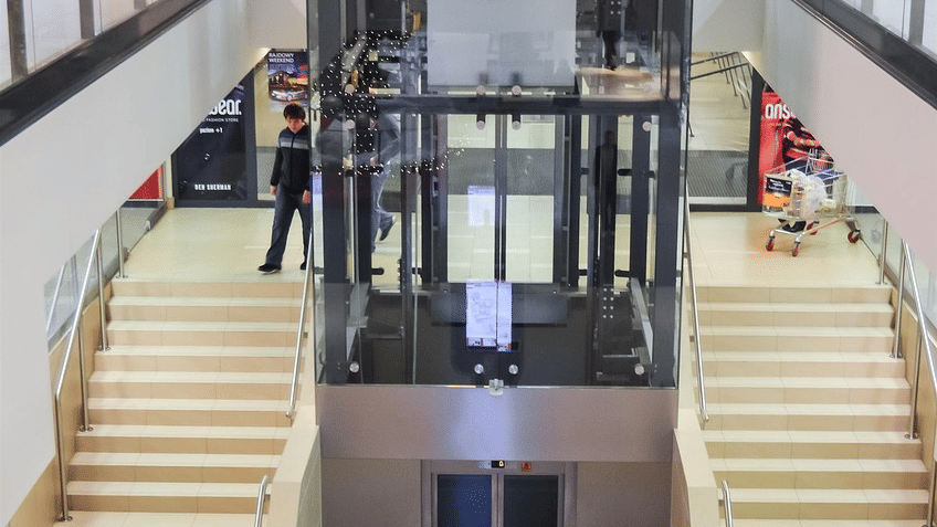 A mall interior showing escalators, stairs, bright lighting, and multiple floors with glass railings and open walkways.