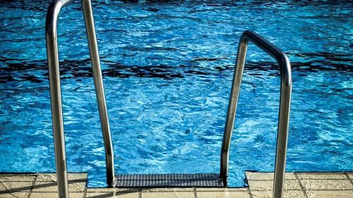 A close-up view shows metal handrails leading into a swimming pool with blue water, bordered by paving stones.