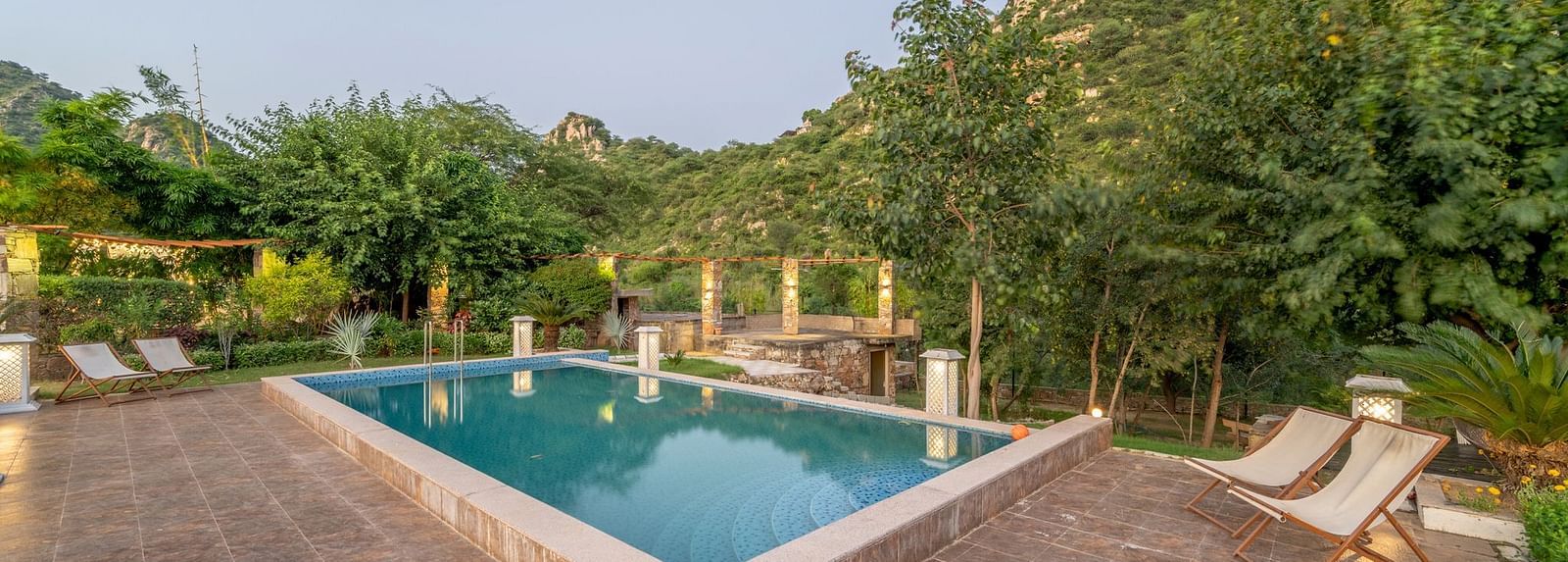 An outdoor pool at Valley by Grassfield, surrounded by plants and trees, with two lounge chairs on the side.