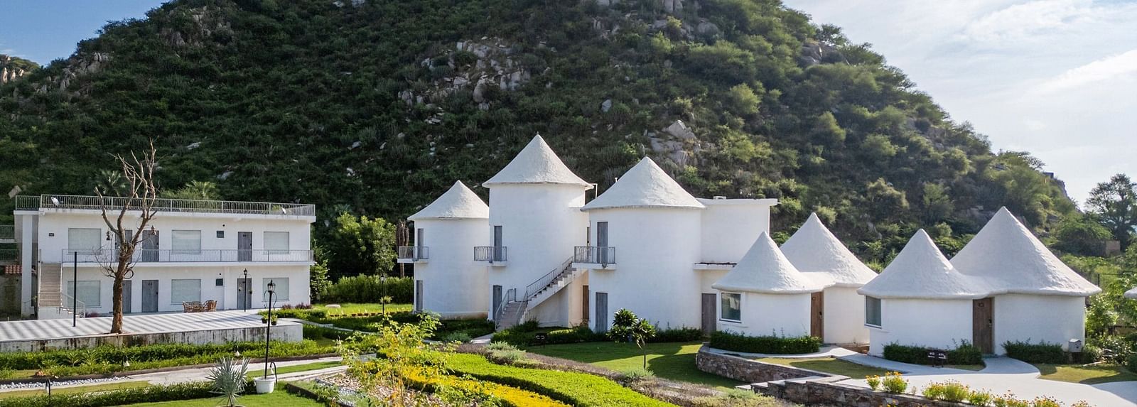 Conical-roof accommodations with an open space in front, set against a scenic mountain backdrop at Valley by Grassfield.