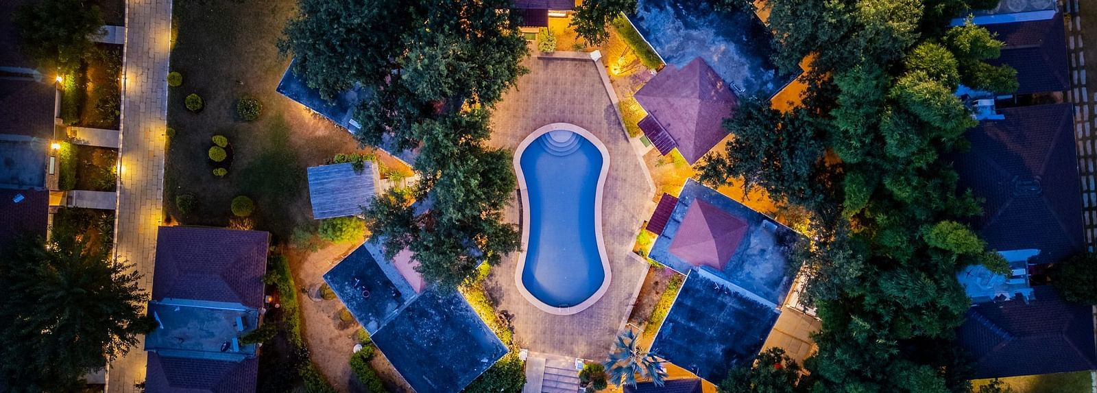 Aerial view of Valley by Grassfield, highlighting the accommodations illuminated by glowing lights, with a swimming pool at the centre.