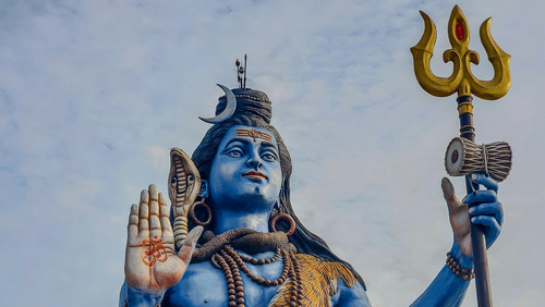 A large, blue statue of Lord Shiva seated with a trident.