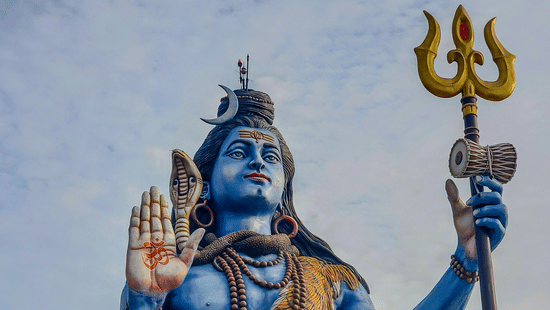 A large, blue statue of Lord Shiva seated with a trident.