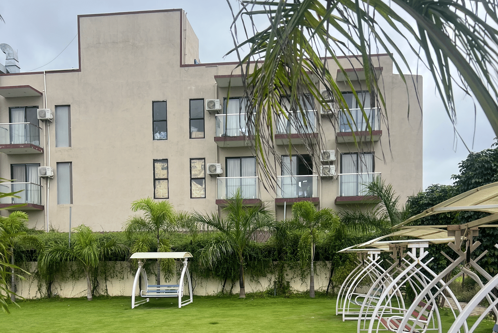 Lawn of Daksh The Valley Resort, Saputara, featuring swings to sit on one side, and the multi-storey resort seen on the other.