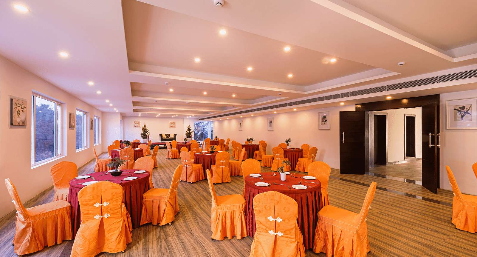 Spacious dining hall with orange chair covers and round tables set for a meal - TGI Grand Fortuna, Hosur
