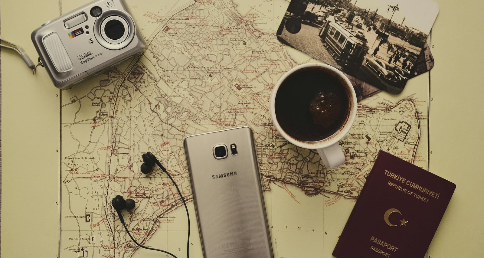 An image of a cellphone, digital camera, coffee mug, and some photographs placed on a table