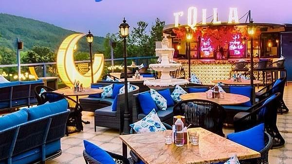 A vibrant rooftop bar at dusk, at TQila Luxury Bar and Multi Cuisine Restaurant featuring comfortable blue seating, warm lighting, and city views, ideal for evening relaxation.