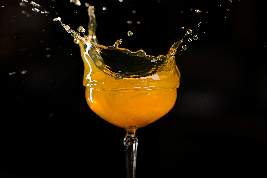 alt-text Fresh orange cocktail splashing in a glass with lime wedges