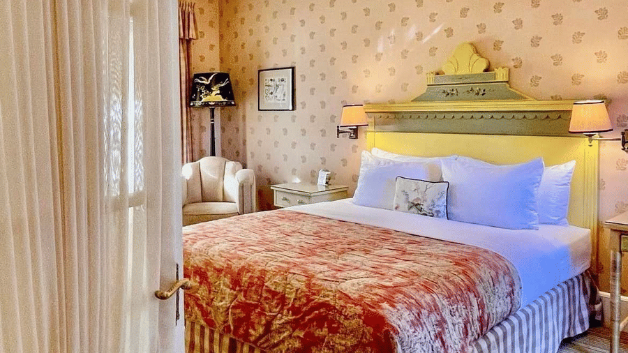Door opening to the bedroom of Lower Garden Room, revealing it's bed, patterned walls, and a sofa at Tallman Hotel