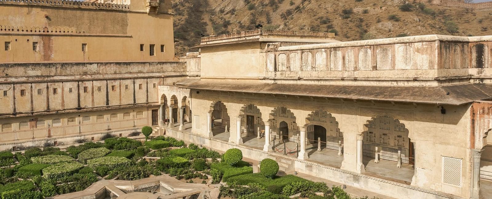A scenic view of Amber Fort in Jaipur, Rajasthan, showcases its intricate architecture, a formal garden with water features, and the surrounding hills.