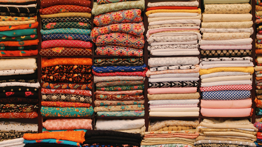 Neatly stacked piles of colourful, patterned fabrics on shelves in a textile shop, with a lone red chair in front.