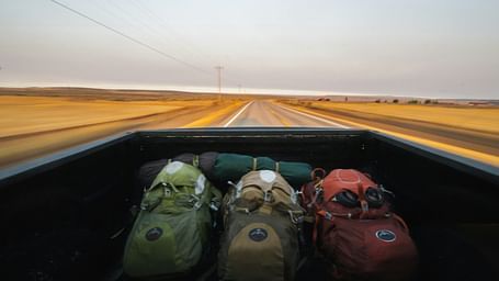 Three backpacks put on the back of a pickup truck and the highway in view.