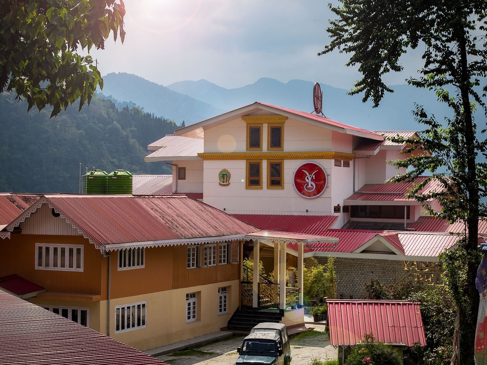 A scenic view of a resort with red rooftops, surrounded by lush greenery and distant mountains under a partly cloudy sky - Yashshree Pelling Chekhim Retreat.