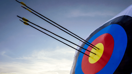 Several arrows hit the centre bullseye of a round target outdoors.