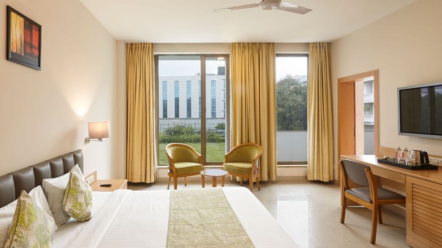 A bright hotel room at Monday Hotels Mahape, Navi Mumbai, with two single beds and large windows.