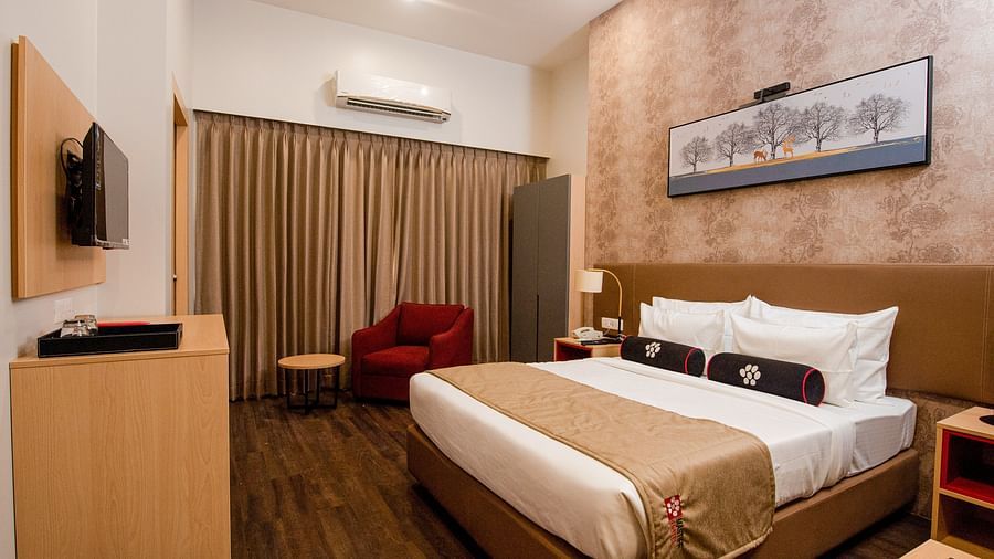 a plush bed with warm toned interiors and room amenities - Mastiff Hotel, Ankleshwar