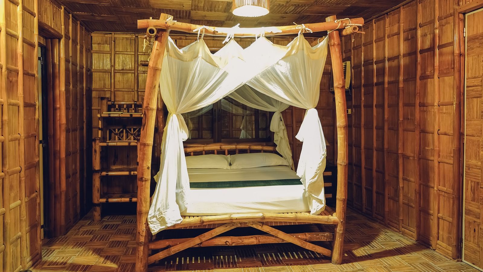 Standard Bamboo Suite at Flower Island Resort featuring a wooden canopy double bed,  bright lighting, and bamboo flooring.
