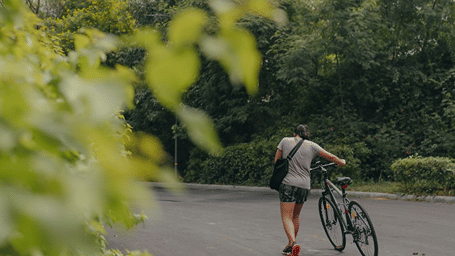 A person holding a cycle and walking on a tarred road - Karma Lakelands.