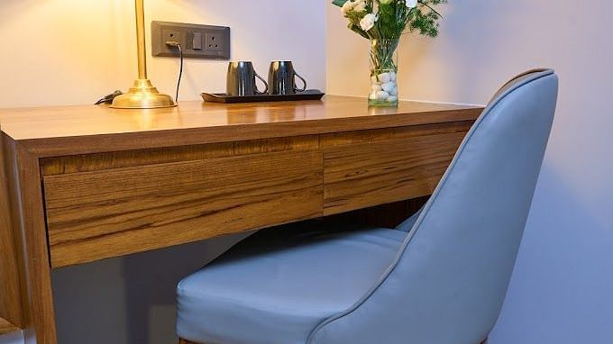 A corner of a room with a lamp and a flower vase placed on a table and a chair infront of it for comfortable seating