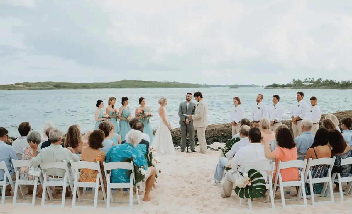 Beach wedding ceremony with guests seated on white chairs, facing the couple under an open sky with the sea behind | Abaco Inn