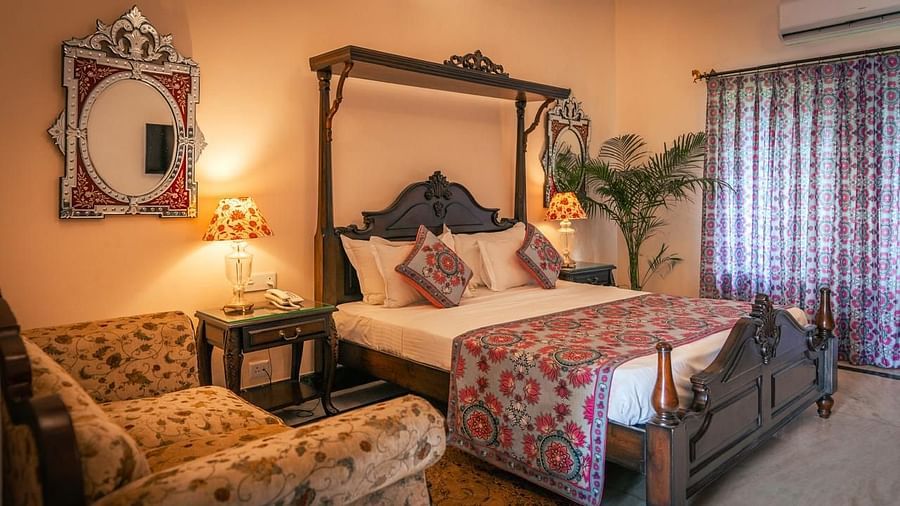 A Deluxe Room with a four-poster bed, a window, a sofa, and elegant decor with warm lighting - Khas Bagh, Jaipur