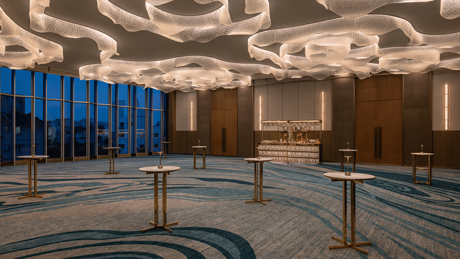 The empty banquet hall Ballroom 2 with swirling modern ceiling lights and high cocktail tables set up near floor-to-ceiling windows at The Residency Towers Chennai.