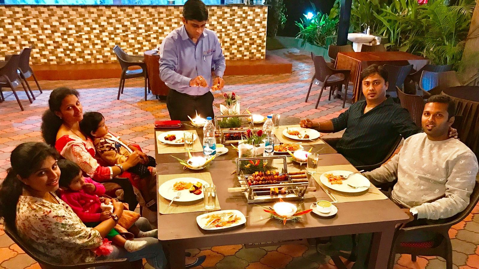 Image of a group of people sitting in front of a table filled with food at Parampara Resort & Spa, Kushalnagar.