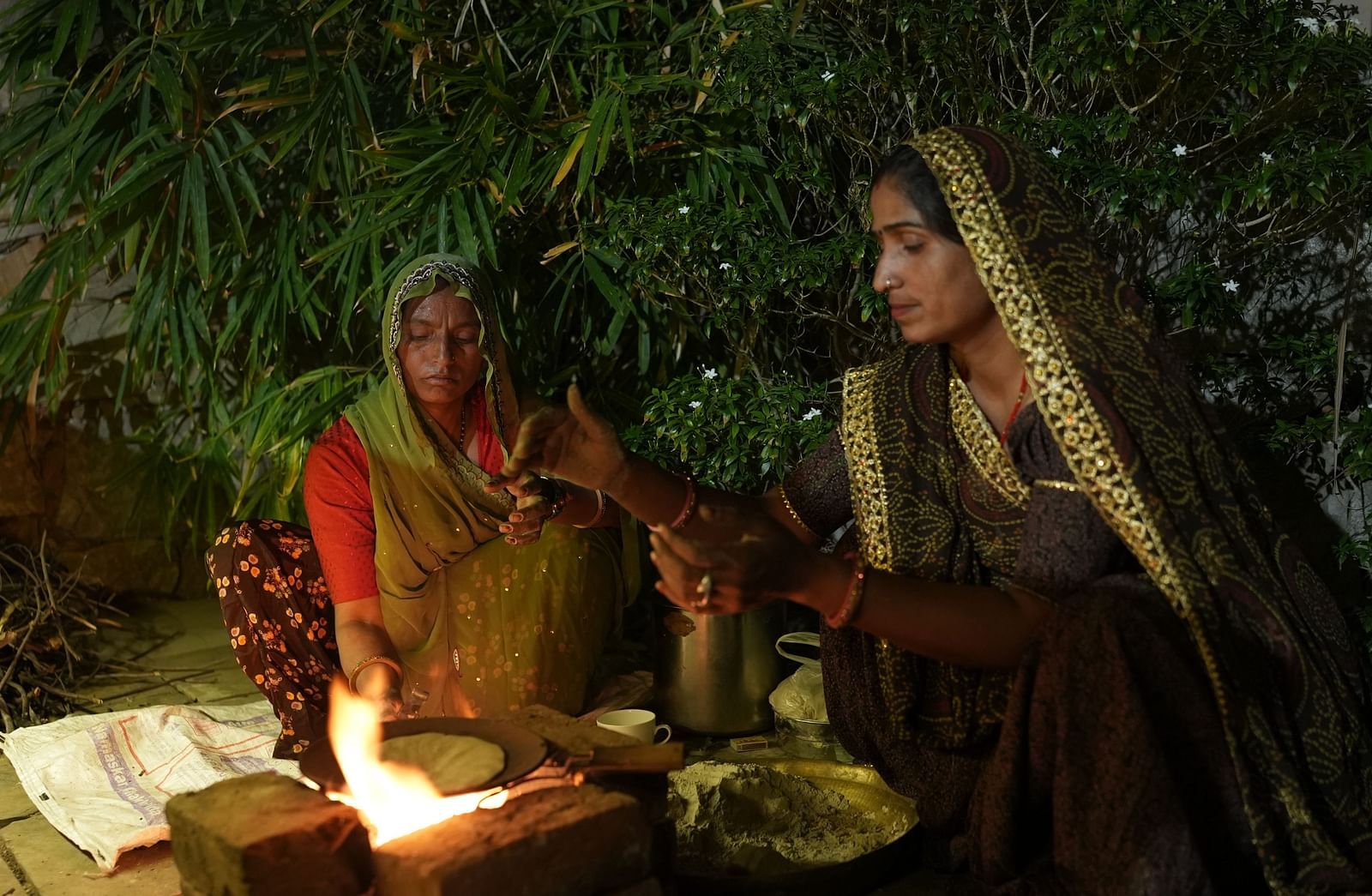 Village women dressed in traditional attire cooking over a fire under a leafy canopy - Khas Bagh, Jaipur.