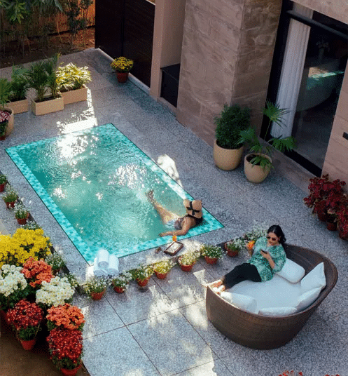 Outdoor hot tub surrounded by plants and seating, placed on a private stone patio with flower pots at Karma Chalets.