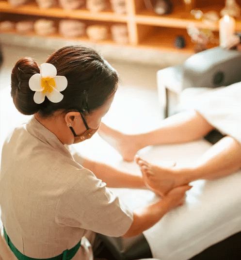 Spa therapist giving a foot massage in a peaceful, warmly lit wellness room at Karma Chalets.