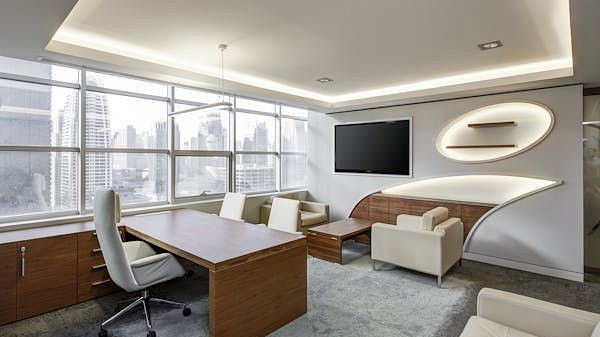 A spacious office with a large desk, chairs, and a seating area by the window.